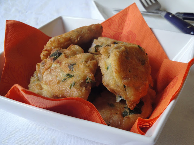 Frittelle dorate con erbe aromatiche servite in un piatto bianco su un tovagliolo arancione, atmosfera calda e rustica.